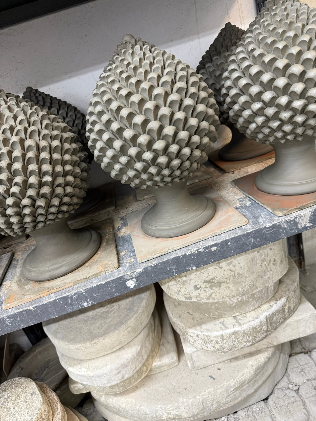 Several gray stone pineapple garden ornaments displayed on a workbench with stone blocks underneath.